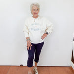 Woman wearing a white sweatshirt with 'Favorite Grandma' text, standing against a white wall.