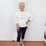 Woman wearing a white sweatshirt with 'Favorite Grandma' text, standing against a white wall.
