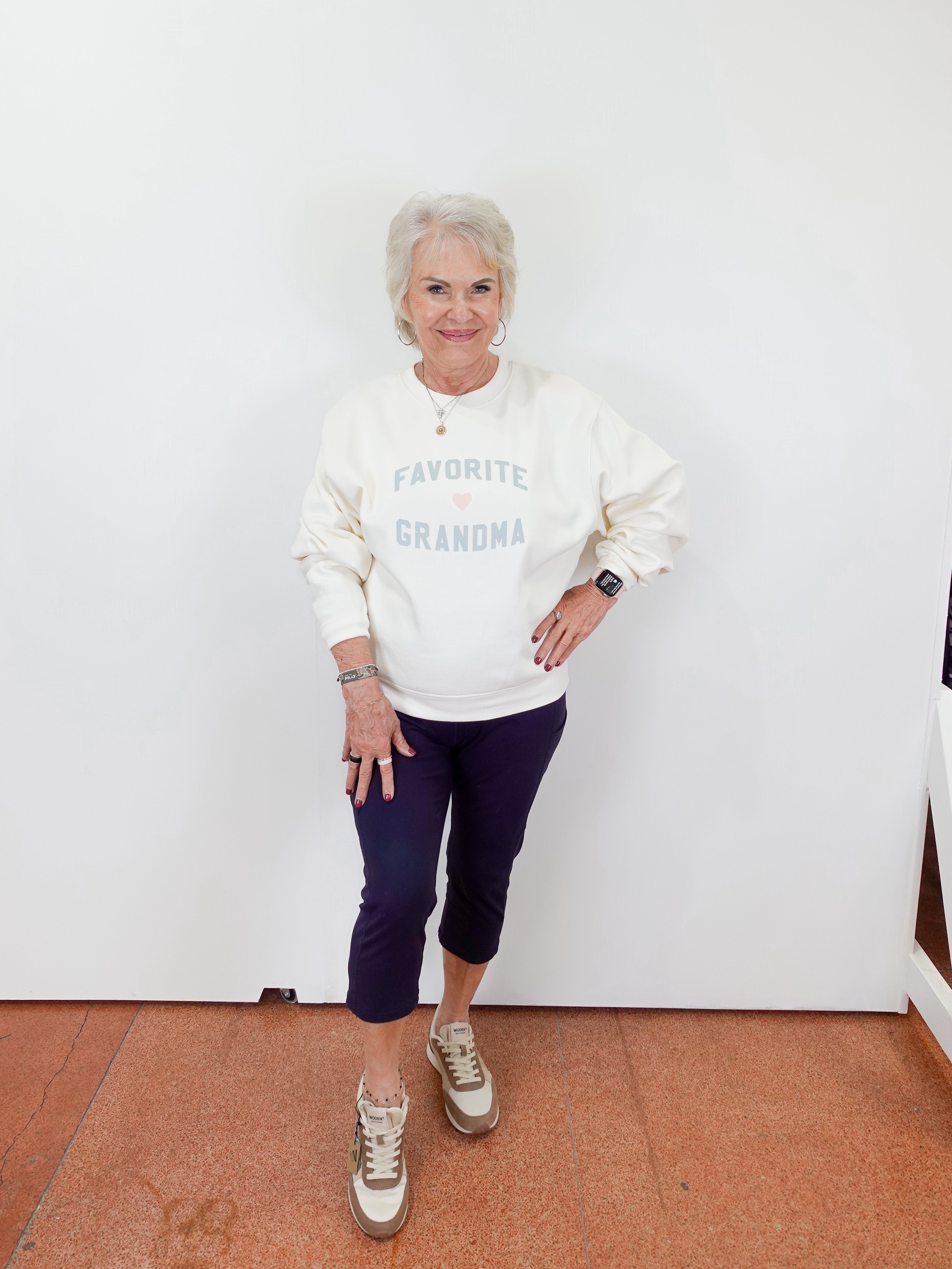 Woman wearing a white sweatshirt with 'Favorite Grandma' text, standing against a white wall.