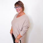 A woman wearing a v-neck jewel embellished sweater in front of a white wall.