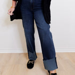Person wearing dark blue jeans and black loafers on a light wooden floor.