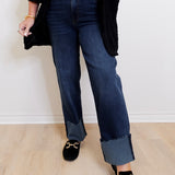 Person wearing dark blue jeans and black loafers on a light wooden floor.