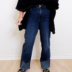 Person wearing dark blue jeans and black shoes on a light wooden floor.