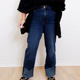 Person wearing dark blue jeans and black shoes on a light wooden floor.