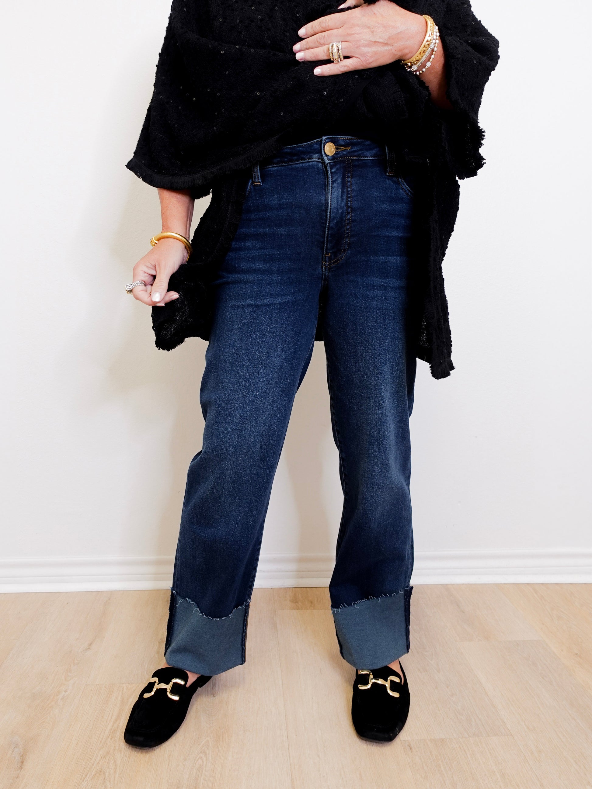 Person wearing dark blue jeans and black shoes on a light wooden floor.