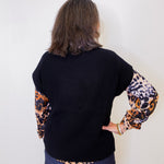 Person wearing a black sweater with leopard print sleeves underneath against a white background