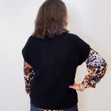 Person wearing a black sweater with leopard print sleeves underneath against a white background