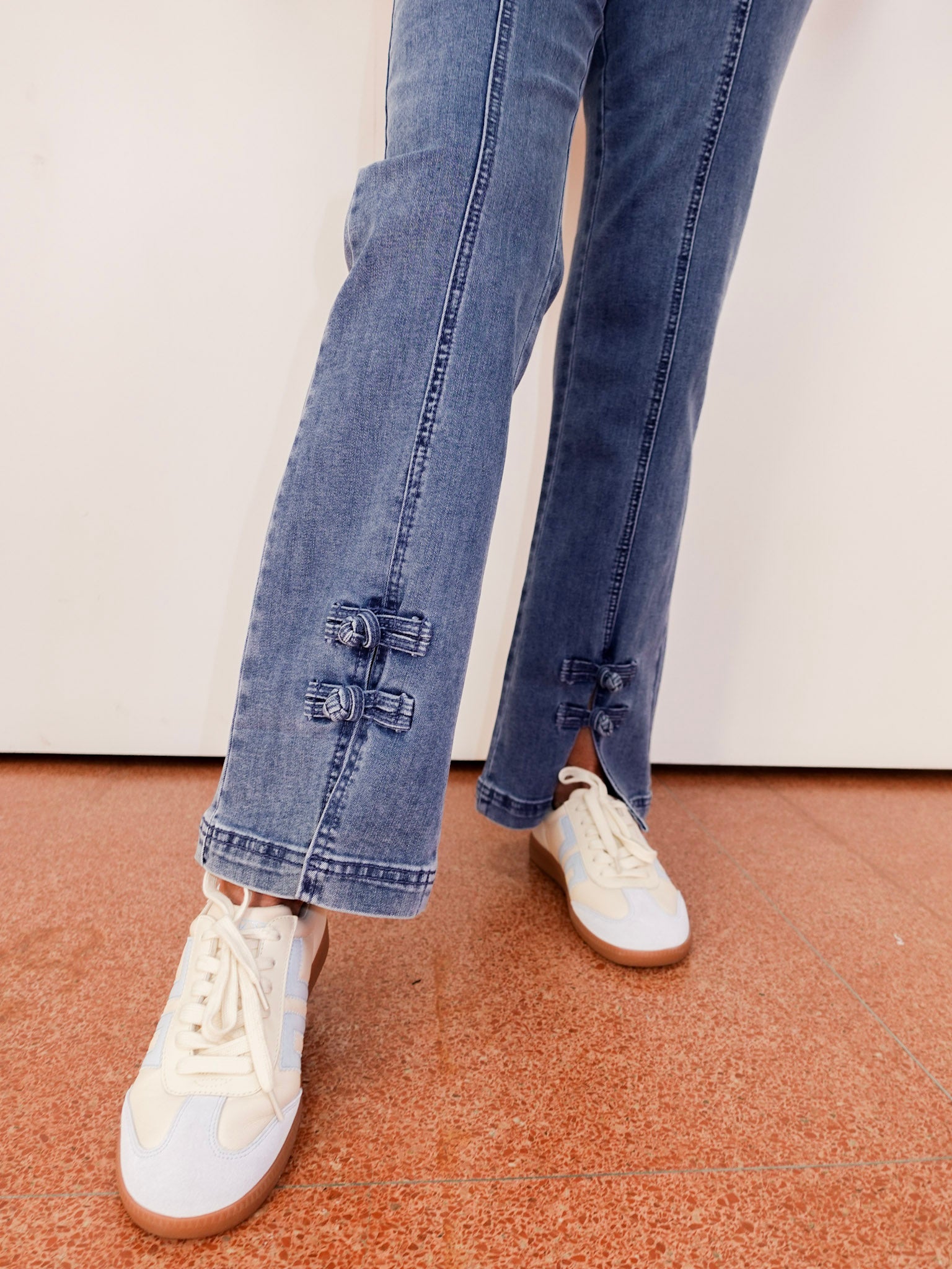 Person wearing blue jeans and white sneakers on a neutral background