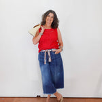 Woman wearing a red top and blue jeans against a white wall.