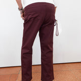 A person shown from the back wearing burgundy straight-leg pants, a white top, and black sandals, standing against a white wall with terracotta tiled flooring.