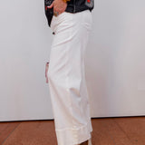 Person wearing white pants and a black jacket with colorful patterns against a white wall.