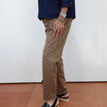 A person shown from the waist down wearing tan straight-leg pants, a navy blue top, and black platform slide sandals against a white wall and terracotta floor.