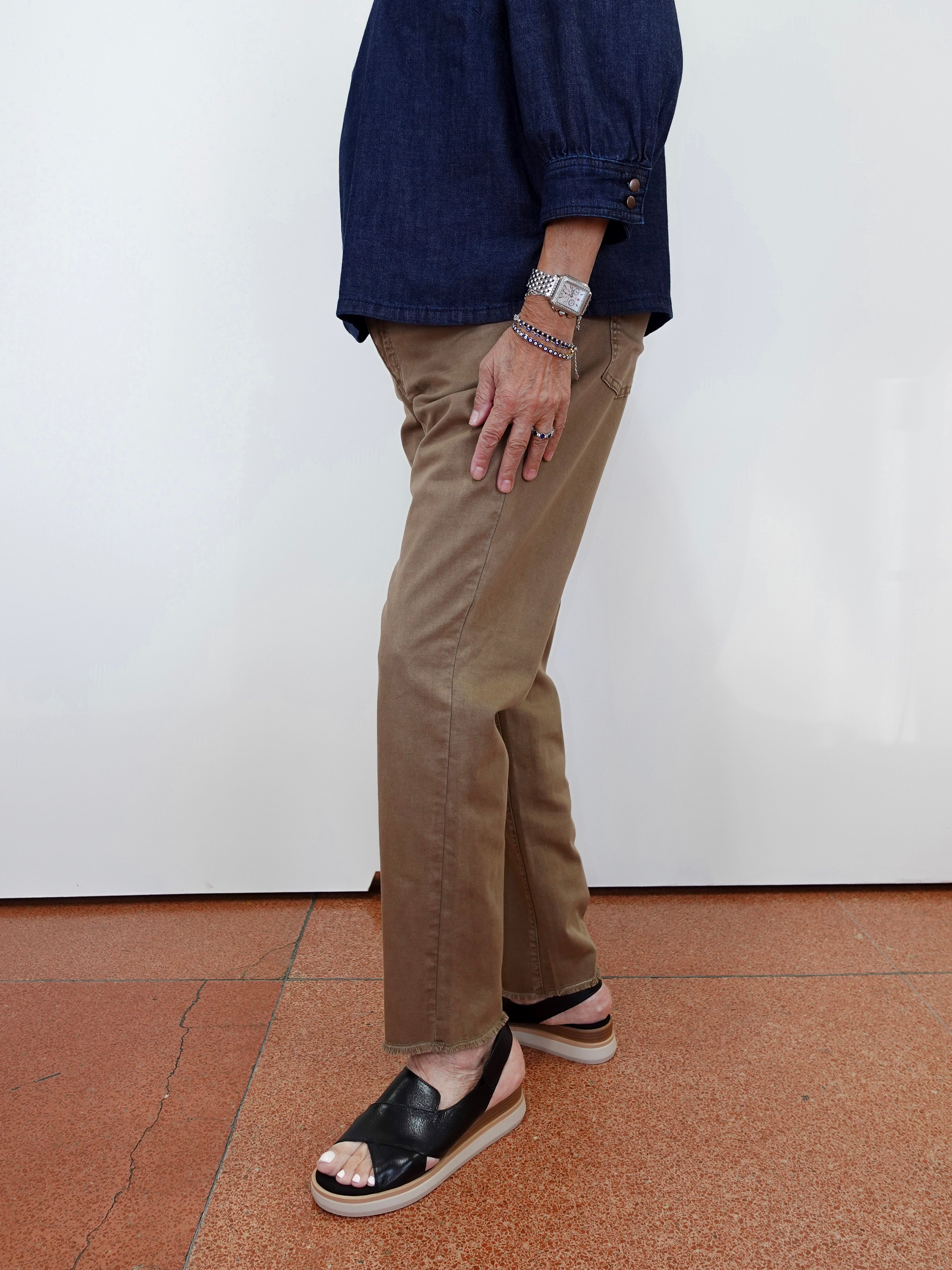 A person shown from the waist down wearing tan straight-leg pants, a navy blue top, and black platform slide sandals against a white wall and terracotta floor.