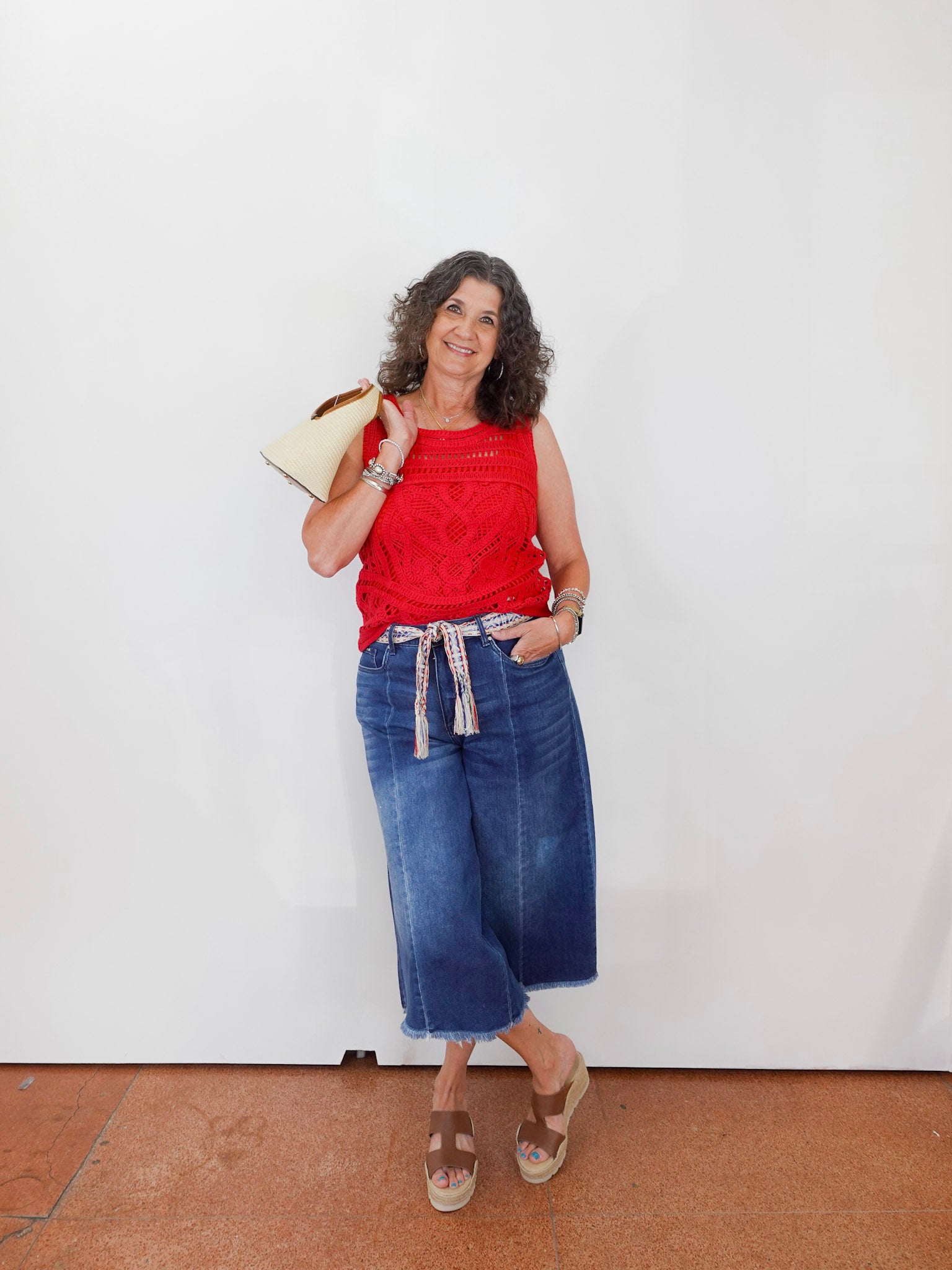 Woman wearing a red top and blue jeans against a white wall.