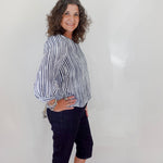 Woman wearing a striped shirt and dark pants against a white wall