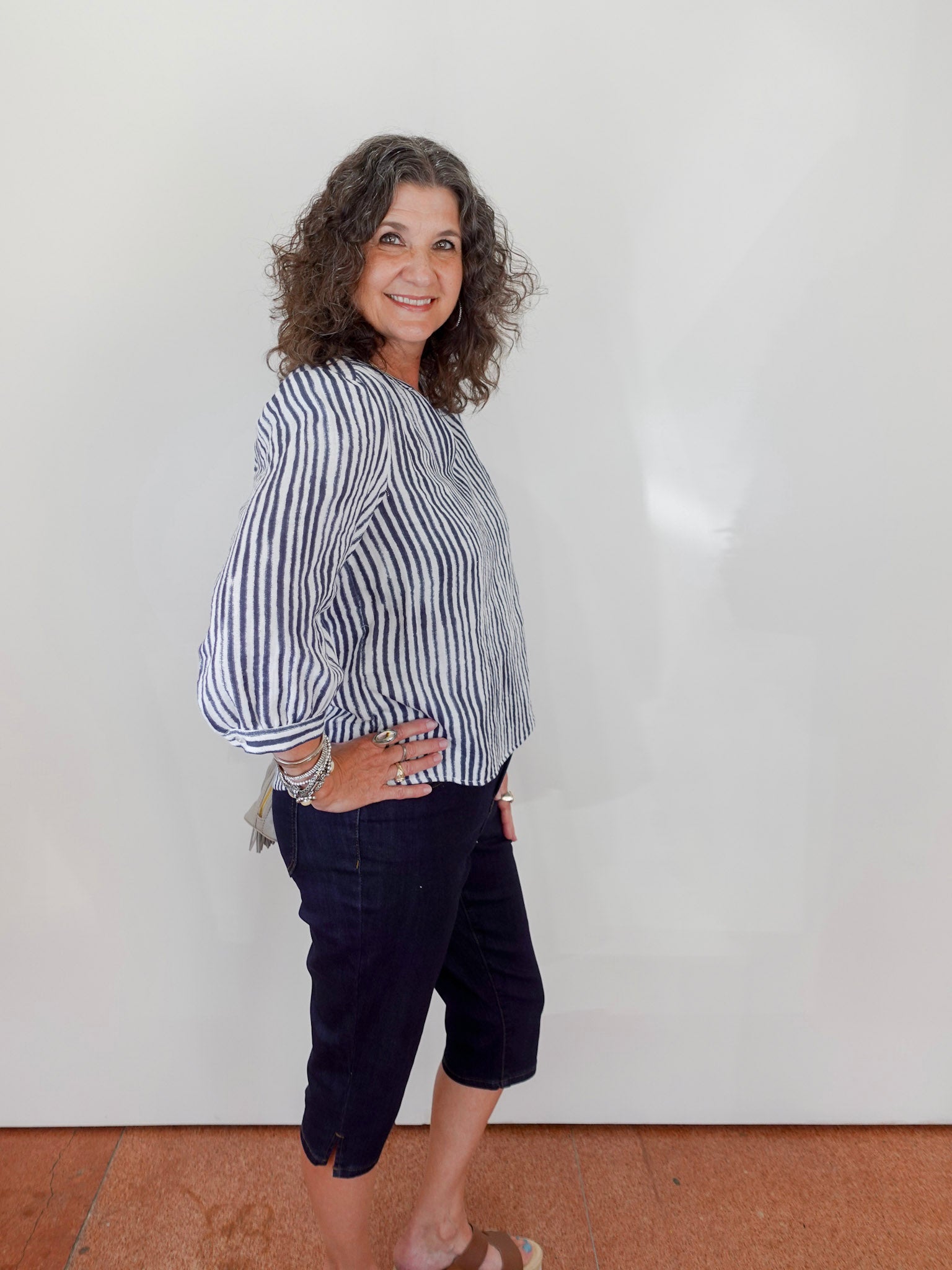 Woman wearing a striped shirt and dark pants against a white wall