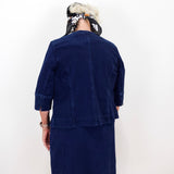 A person shown from the back wearing a dark navy blue corduroy jacket and matching skirt set against a plain white wall.