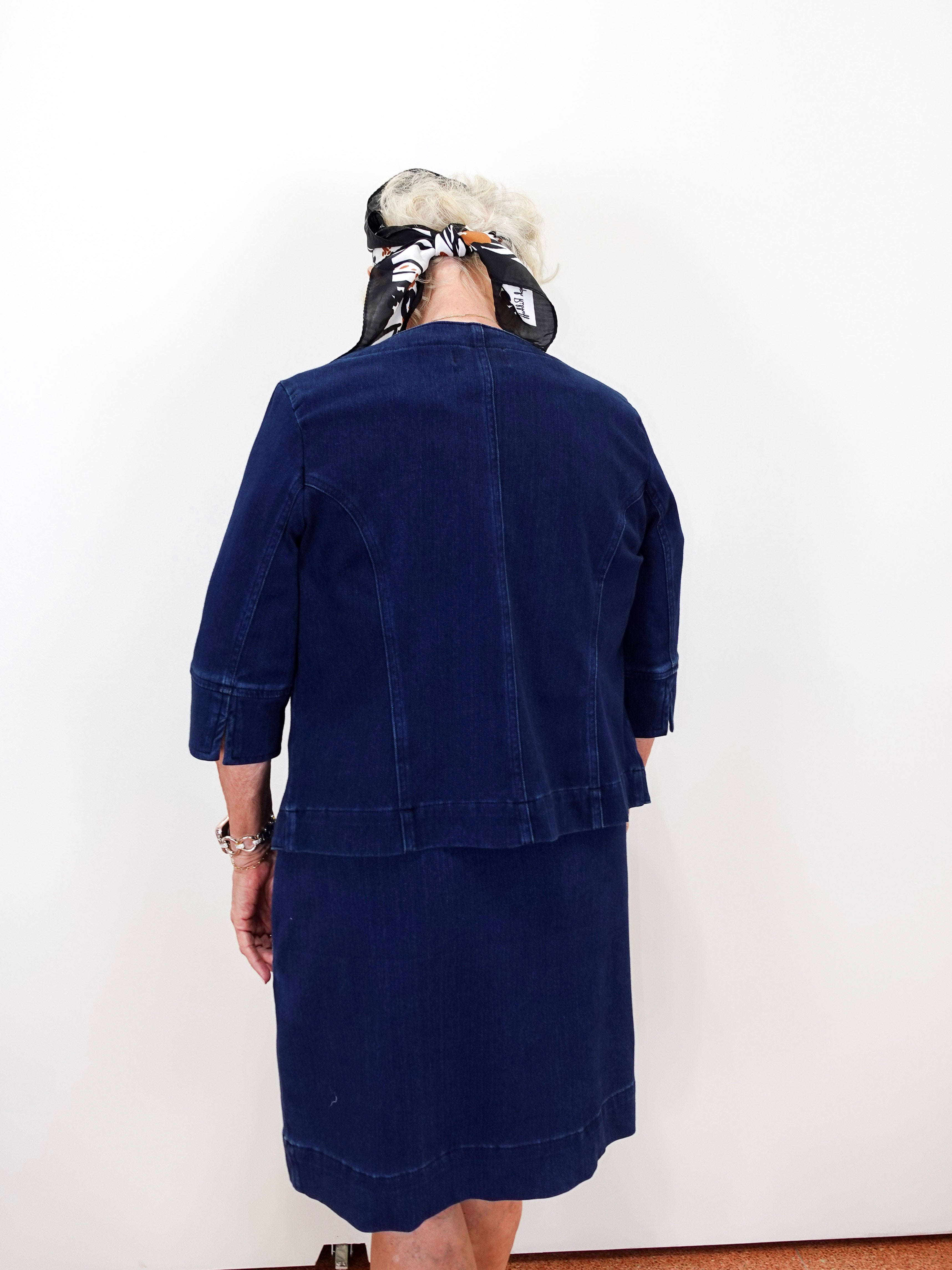 A person shown from the back wearing a dark navy blue corduroy jacket and matching skirt set against a plain white wall.