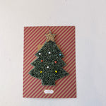 Christmas tree-shaped brooch on a striped card with a white background