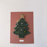 Christmas tree-shaped brooch on a striped card with a white background