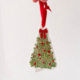 Hand holding a Christmas tree ornament with red berries and a red ribbon against a white background