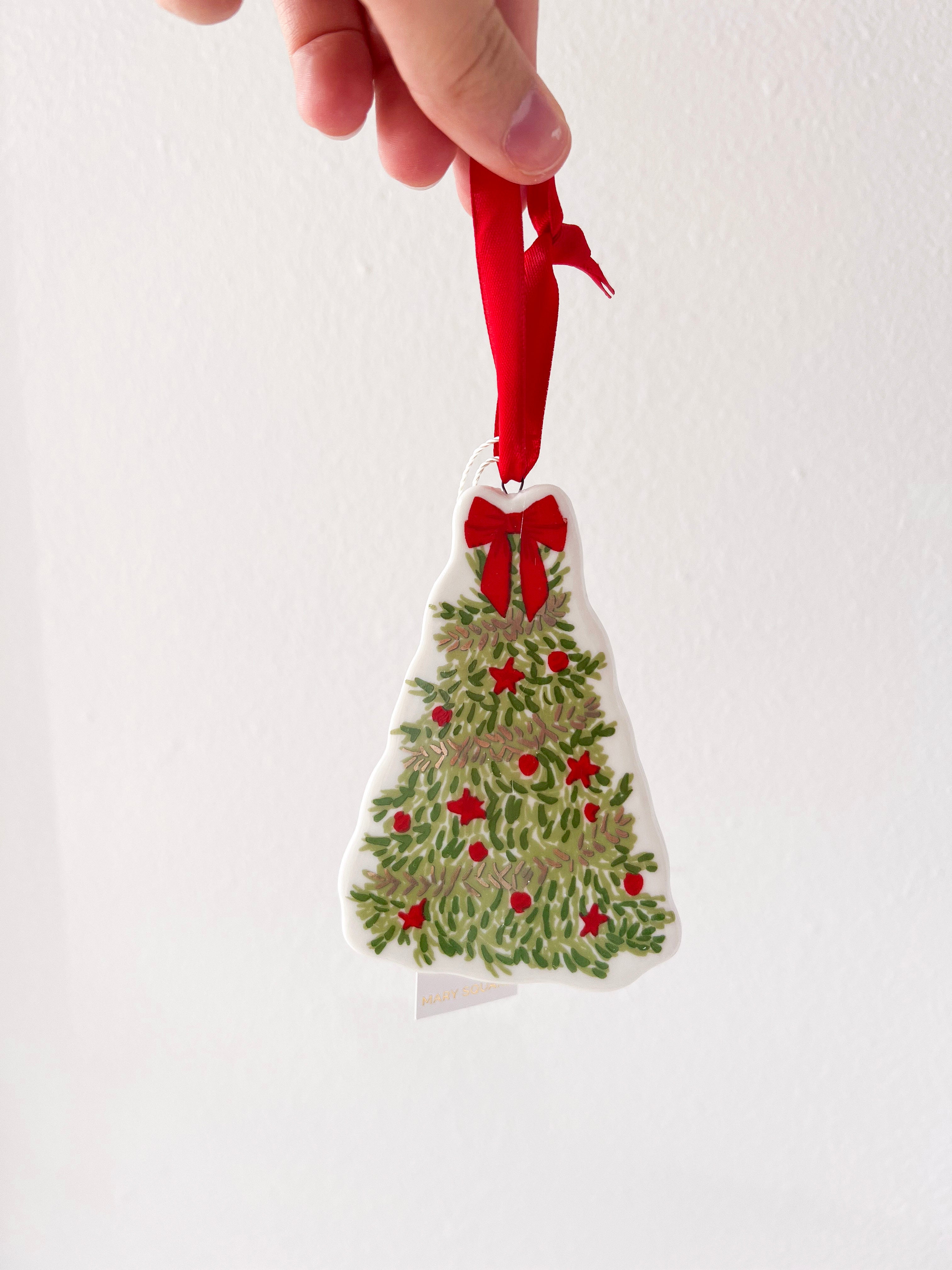 Hand holding a Christmas tree ornament with red berries and a red ribbon against a white background