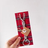 Red plaid napkin with a bottle opener and tag held by a hand on a white background