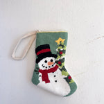Small knitted stocking with a snowman design on a light gray background