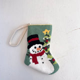 Small knitted stocking with a snowman design on a light gray background