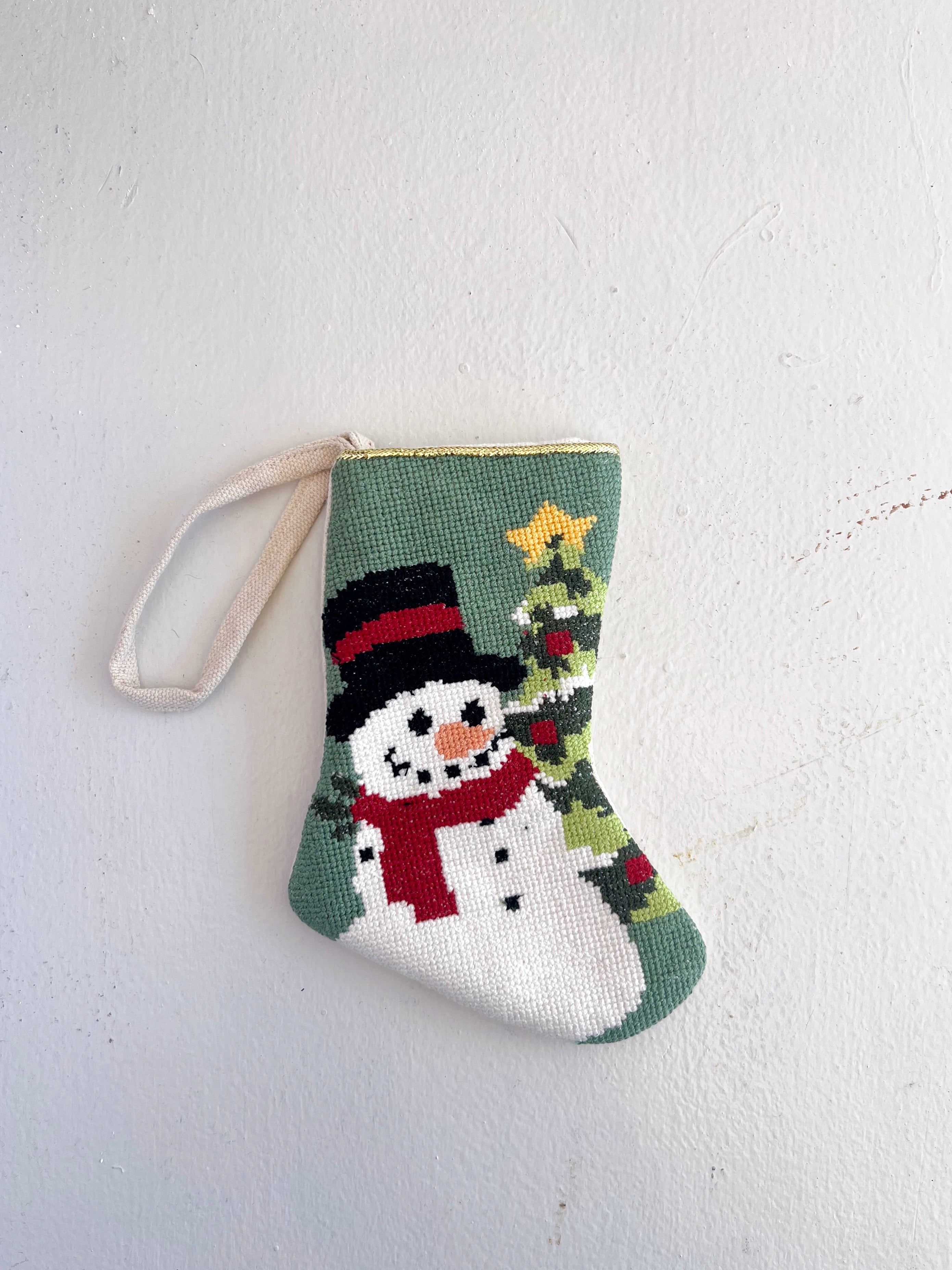 Small knitted stocking with a snowman design on a light gray background
