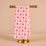 Towel with red bow pattern on a gold towel rack against a beige background