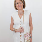 Woman in a white dress with gold buttons holding a floral handbag against a white background