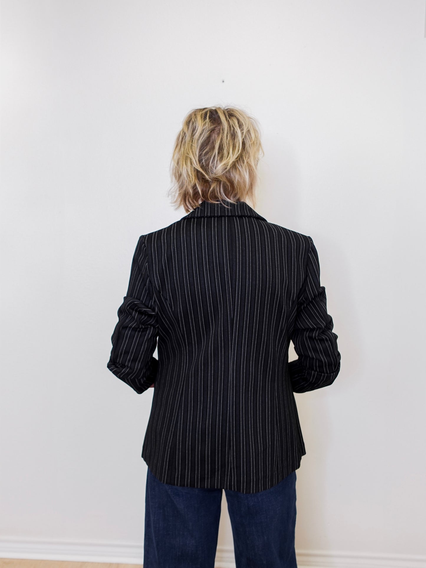 Person wearing a black pinstripe blazer against a white wall