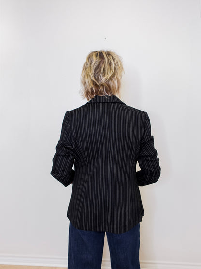 Person wearing a black pinstripe blazer against a white wall
