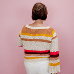 Person wearing a colorful striped sweater against a pink background
