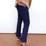 A person wearing navy blue cropped trousers, a beige striped top, and navy espadrille sandals, standing against a white wall.