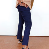 A person wearing navy blue cropped trousers, a beige striped top, and navy espadrille sandals, standing against a white wall.
