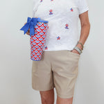 Person wearing a white t-shirt with red, blue, and yellow designs, holding a red, white, and blue patterned cup.