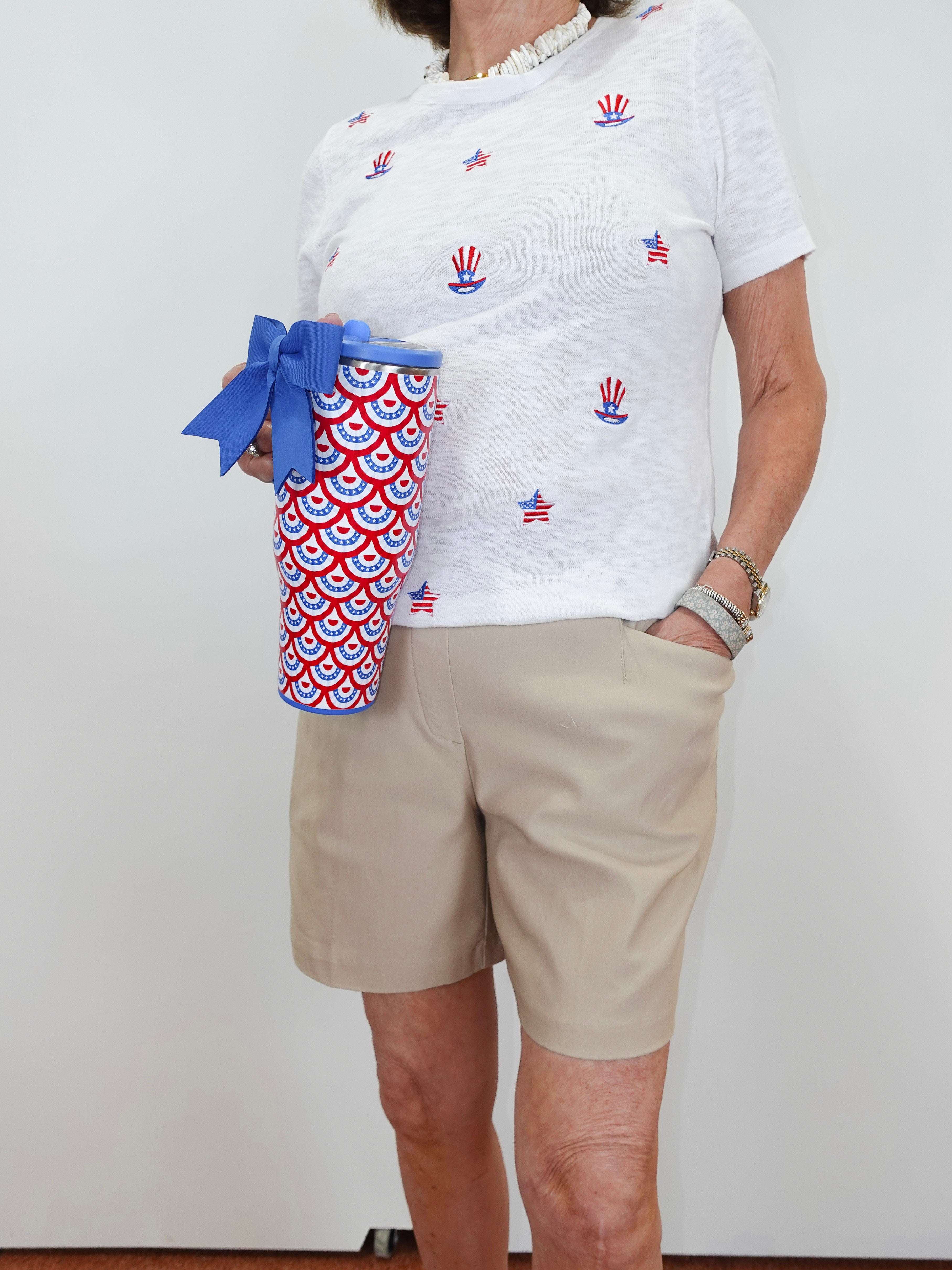 Person wearing a white t-shirt with red, blue, and yellow designs, holding a red, white, and blue patterned cup.