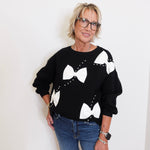 Woman wearing a black sweater with white bow patterns against a plain background