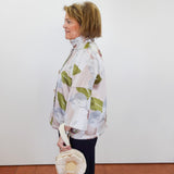 Woman wearing a patterned jacket holding a round bag against a white wall.