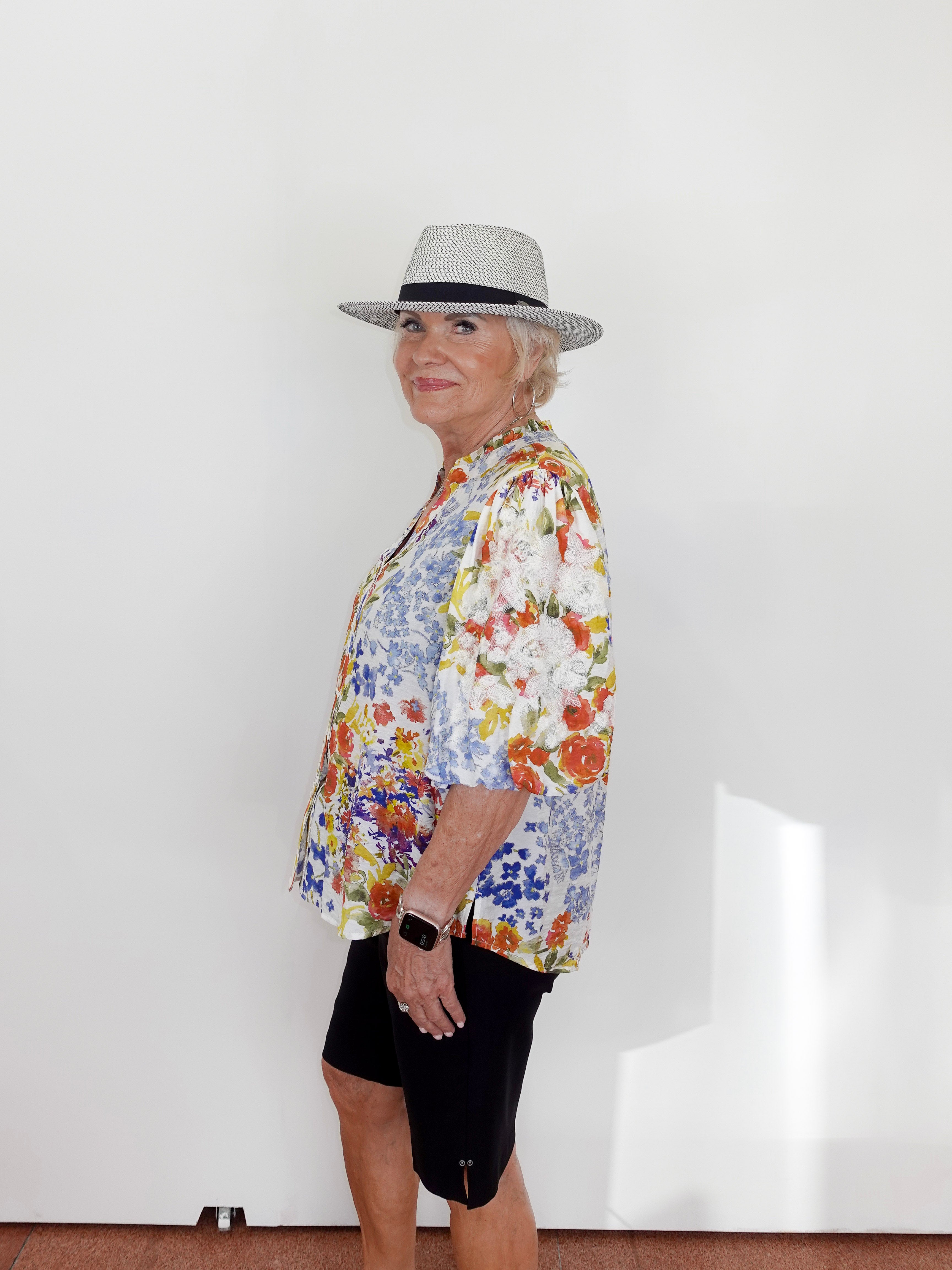 Person wearing a colorful floral shirt and black shorts with a gray hat against a white wall.