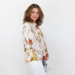 Woman wearing a floral blouse and white skirt against a plain background