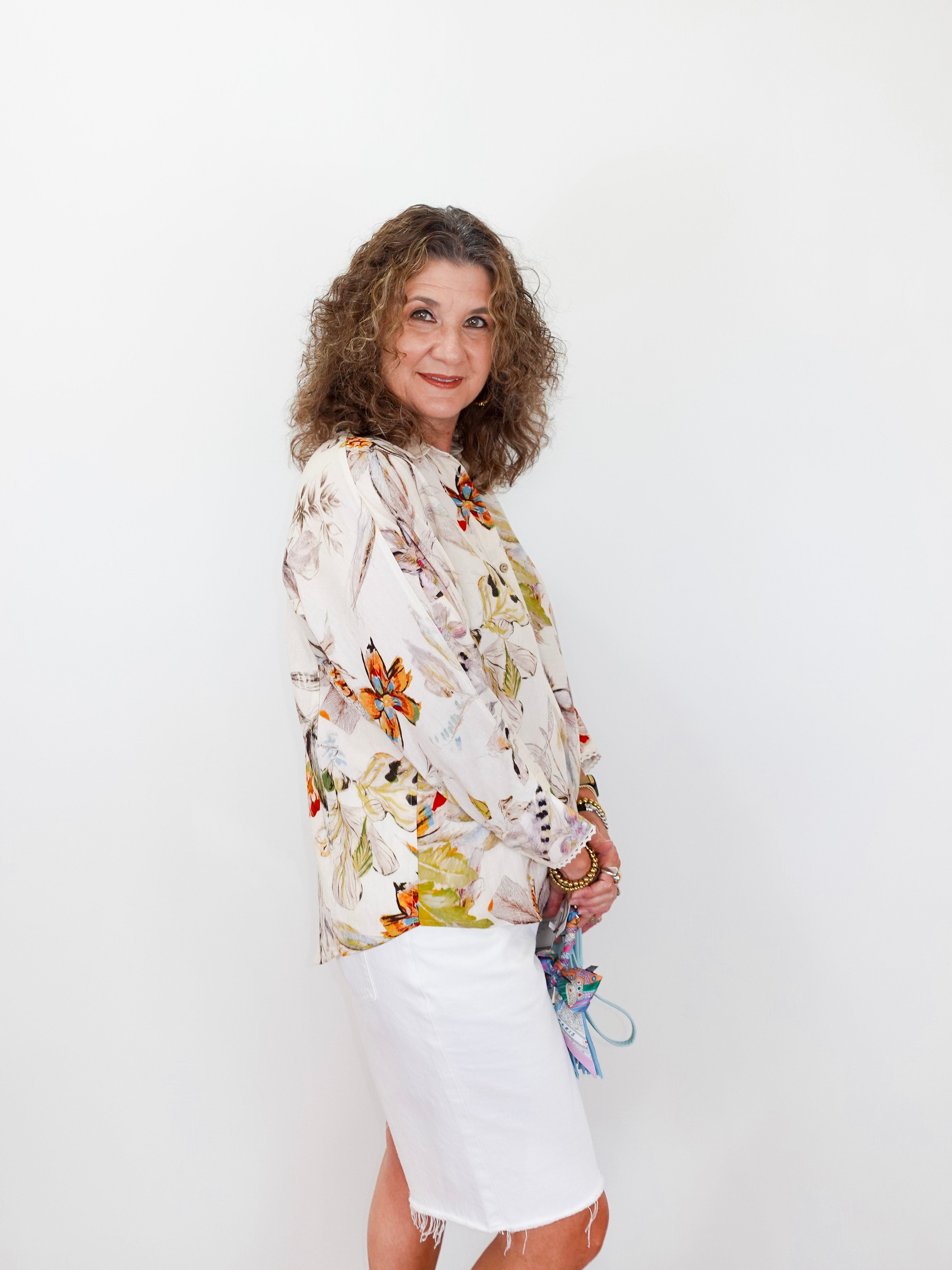 Woman wearing a floral blouse and white skirt against a plain background