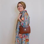 Woman wearing a floral dress holding a brown handbag against a plain background