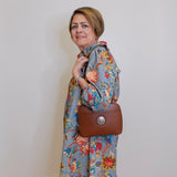 Woman wearing a floral dress holding a brown handbag against a plain background