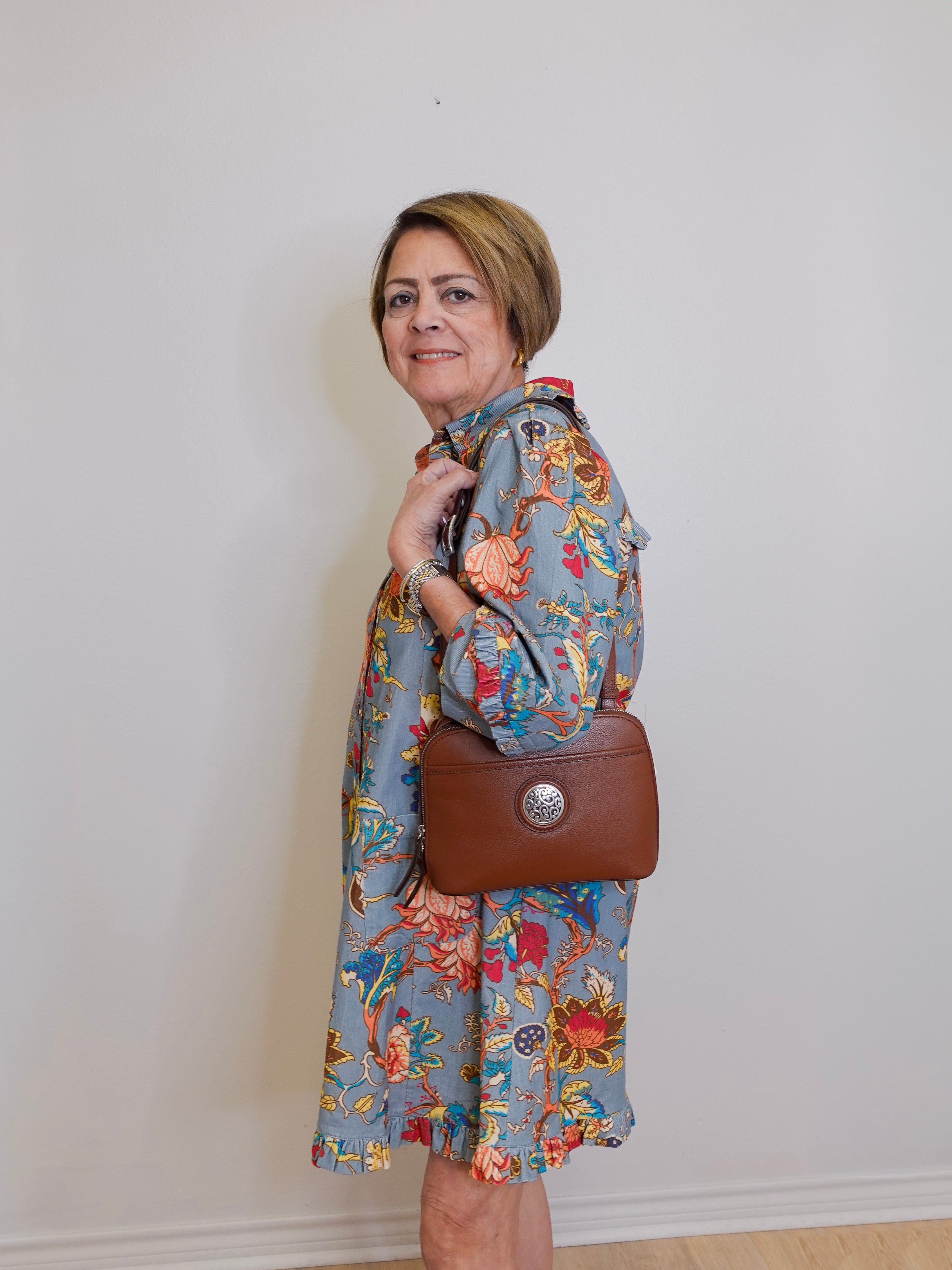 Woman wearing a floral dress holding a brown handbag against a plain background