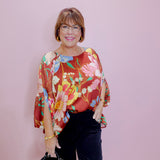 Woman wearing a colorful floral blouse and black pants against a pink background