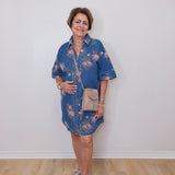 Woman wearing a blue floral dress with a beige bag against a white wall.