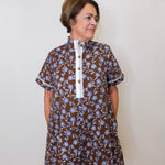 Woman wearing a brown floral dress with a white collar against a plain background